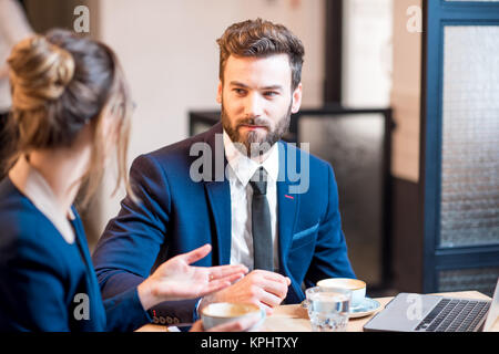 Conversation between business couple dressed in suits sitting with coffee at the cafe or restaurant Stock Photo