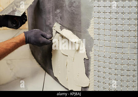 Installation of mosaic tiles. The worker puts adhesive on the base Stock Photo