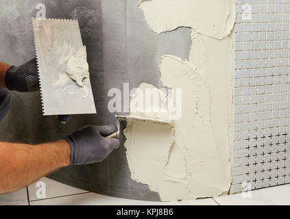 Installation of mosaic tiles. The worker puts adhesive on the base Stock Photo