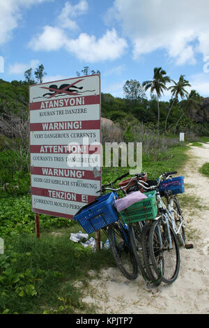 Bicycles and strong current warning sign near forest, La Digue Island, Seychelles. Stock Photo