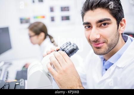 Male scientist using microscope, looking at camera. Stock Photo