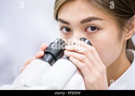 Female scientist using microscope, looking at camera. Stock Photo