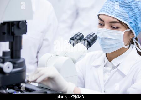Female scientist wearing protective mask using microscope. Stock Photo
