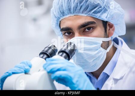 Male scientist wearing surgical cap using microscope. Stock Photo