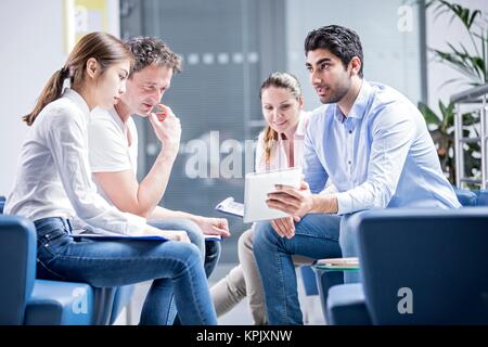 Colleagues having meeting on sofa, young man with digital tablet. Stock Photo