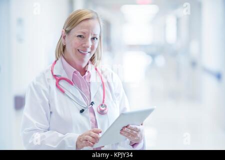 Mature nurse using digital tablet in hospital, smiling. Stock Photo