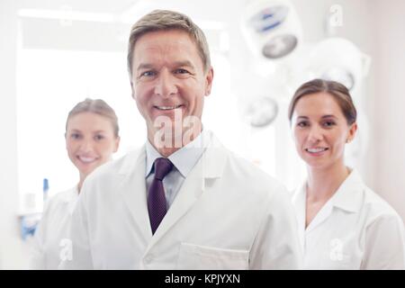 Male doctor smiling towards camera, two doctors in the background. Stock Photo