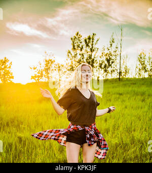 A young woman with long blond hair twirls and runs freely in a grass field in a park; Edmonton, Alberta, Canada Stock Photo