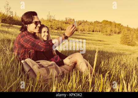 Young couple in a park posing for a self-portrait with their cell phone; Edmonton, Alberta, Canada Stock Photo
