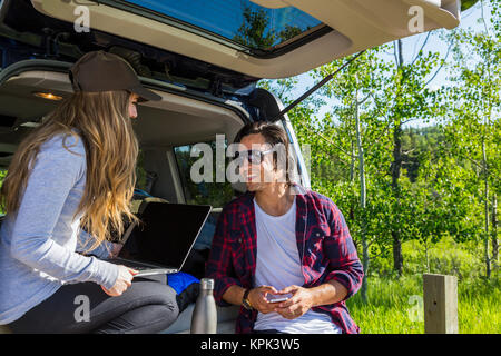 Young couple at their vehicle with the back open looking at a laptop computer; Edmonton, Alberta, Canada Stock Photo
