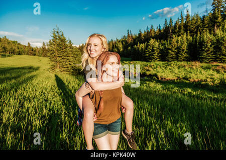 Two friends walking in a park, one giving the other a piggy back ride; Edmonton, Alberta, Canada Stock Photo
