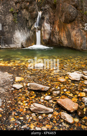 A double waterfall between dark rock walls with the foreground of colourful small rocks and pebbles; Calgary, Alberta, Canada Stock Photo