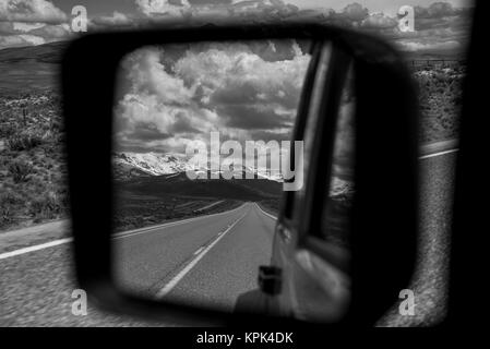 View of the highway and mountains,behind from a vehicle's rear view mirror out the side of the driver's door Stock Photo