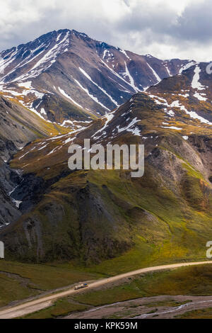 A truck approaches Atigun Pass along the Dalton Highway with the mountains of the Brooks Range towering overhead; Alaska, United States of America Stock Photo