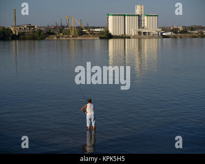 A man stands in knee-deep water in the Danube river fishing in his shorts and sleeveless shirt; Kladovo, Bor District, Serbia Stock Photo