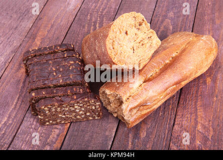Assorted fresh breads, slice and knife isolated on old wood table. Stock Photo