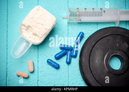 Container of milk whey protein, injection and disc from dumbbell. Close-up. Blue background Stock Photo