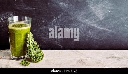 Single cabbage leaf leaning against tall glass filled with green smoothie beverage over wooden table and black background with copy space Stock Photo