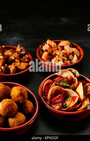 Four round ceramic bowls of delicious traditional Spanish tapas on black background Stock Photo