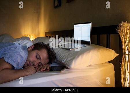 Portrait of young caucasian tired man laying on bed using laptop for a long time. Stock Photo