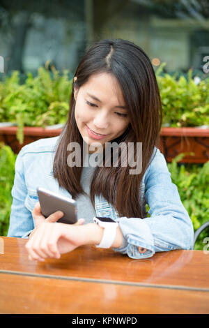 Woman using cellphone and smart watch at outdoor cafe Stock Photo