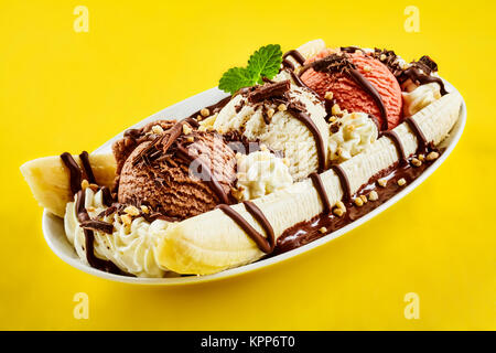 Tropical banana split with chocolate drizzle over three scoops of chocolate, strawberry and vanilla ice cream on fresh bananas, yellow background Stock Photo