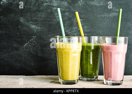 Trio of healthy fruit and vegetable smoothies - berry, kale and banana and almond - with straws on a rustic wooden table with slate background with copy space Stock Photo