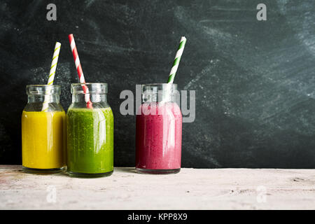 Three mason jars of yellow green and pink tropical fruit drinks with swirl colored straws next to a dusty chalkboard Stock Photo