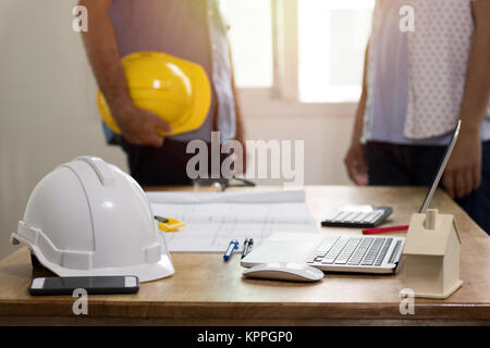 focus at safty helmet on working desk and two engineer standing and dicuss background Stock Photo