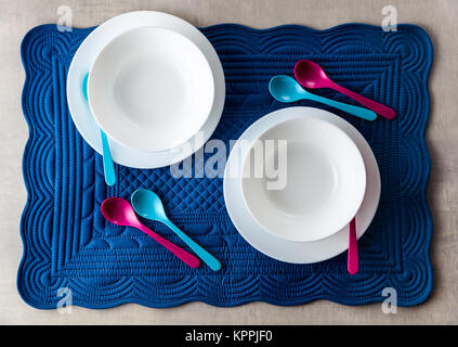 A set of baby dishes on a blue soft napkin for breakfast. kitchen table accessories for serving. Colored small spoons. Stock Photo