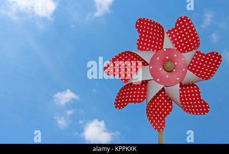 red and white pinwheel with dots against blue sky with some small clouds Stock Photo