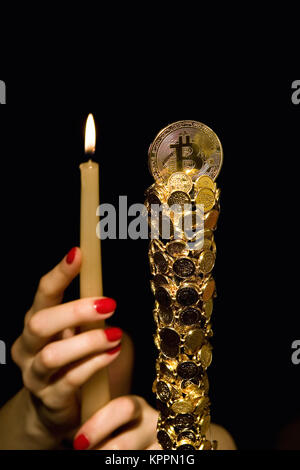 Female hands hold a candle in front of bitkoin. Stock Photo