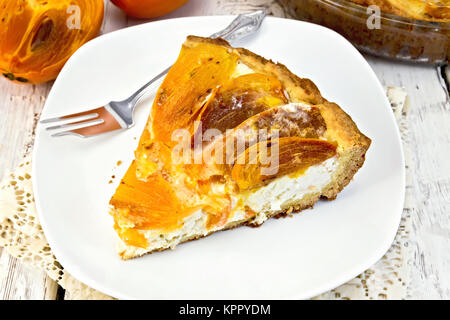 Pie with curd and persimmons with fork in plate on board Stock Photo
