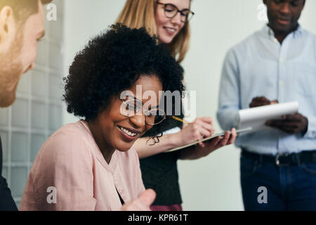 Smiling African businesswoman having a discussion with a colleague while working together in a modern office Stock Photo