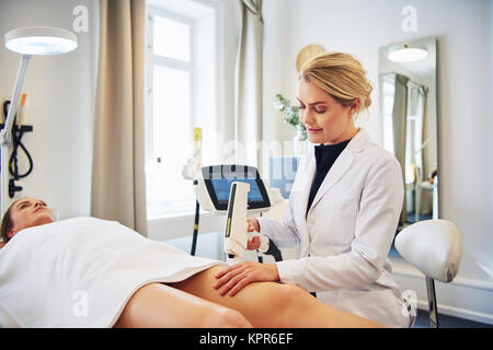 Young female technician performing a laser hair removal procedure on the legs of a young woman lying on a table in a beauty clinic Stock Photo