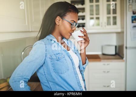 Content young African woman standing alone in her kitchen at home taking a sip from a cup of fresh coffee Stock Photo