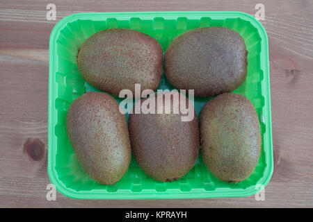 Five Kiwi fruits in a green box isolated on wooden background Stock Photo