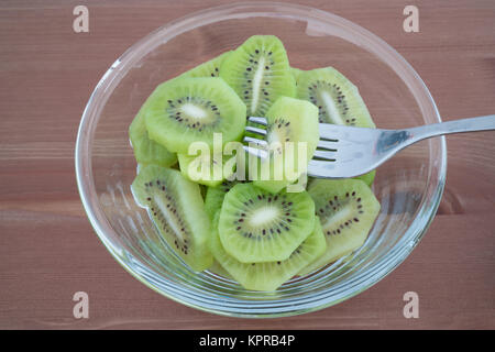 Bowl full with high in vitamins Kiwi fruit slices and fork isolated on wooden background Stock Photo