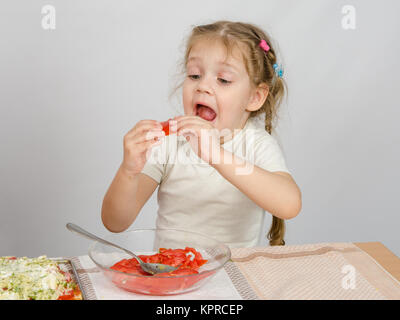 A little girl tries to stick to widely open mouth large slice of tomato Stock Photo