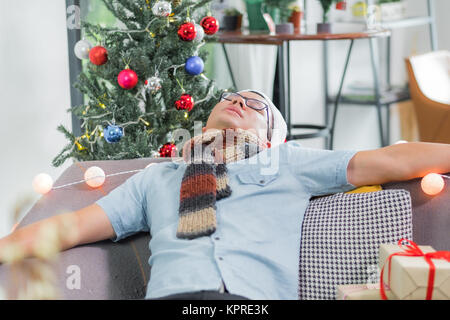 Asia man hangover and passed out sleep on sofa after heavy Christmas and new year party finish and lay on couch until morning,celebration holiday even Stock Photo