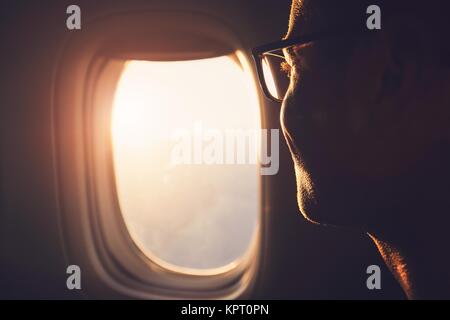 Young passenger looking out through window of the airplane during sunrise. Stock Photo