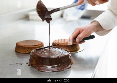 pastry chef covering cake with melted chocolate Stock Photo