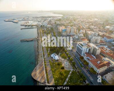 Aerial view of Molos Promenade on the coast of Limassol city in Cyprus. A view of the walk path surrounded by palm trees, pools of water, grass, the Mediterranean sea, piers, rocks urban skyline, old port and Marina. Stock Photo