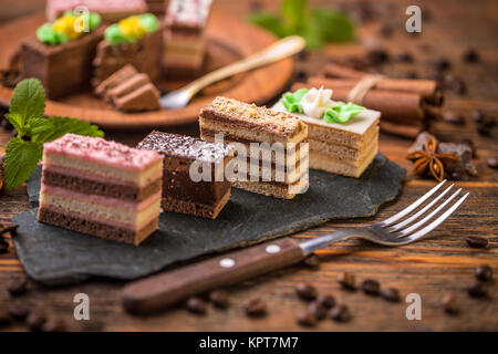Small square cakes with different cream on black slate Stock Photo
