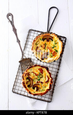 Two tasty seasonal mushroom quiches made with a fresh autumn harvest of fungi, cheese and eggs seasoned with herbs, overhead view of two on a rack Stock Photo