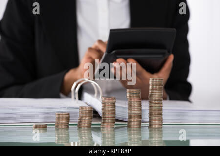 Businesswoman Calculating Invoice With Coins On Desk