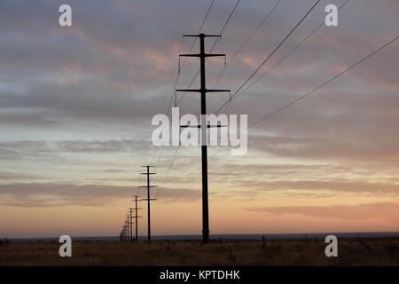 Long row of tall steel electricity pylons and high voltage power lines crossing through the High Plains region of the western United States Stock Photo