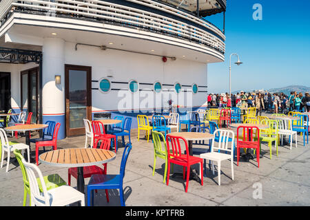 Restaurant patio with colorful chairs at pier 45 in San Francisco, California, USA, with people gathered at the waterfront promenade in the background Stock Photo