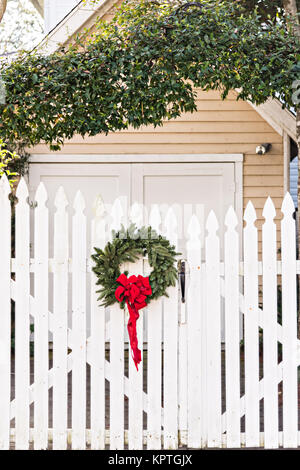 A wooden picket fence of a historic home decorated with a Christmas wreath on Water Street in Charleston, SC. Stock Photo
