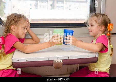 Two little sisters in identical pajamas drinking tea in the train at the table on outboard second-class carriage Stock Photo
